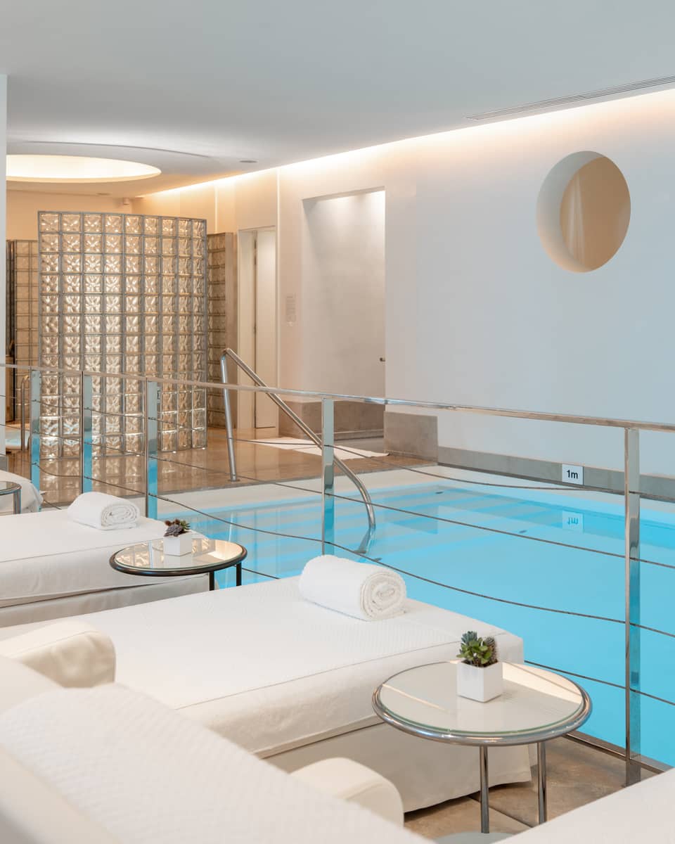A spacious, well-lit indoor pool area with comfortable poolside spa treatment tables