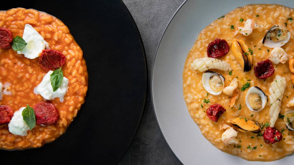 Two risotto dishes, one seafood on white plate and one Italian on black plate