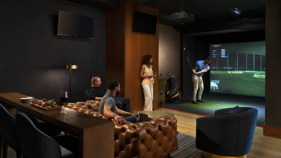 A group of people enjoying an indoor golf simulator experience at the luxury hotel Topgolf Swing Suite, with plush seating and a relaxed atmosphere