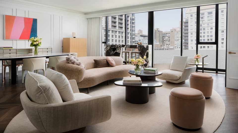 Hotel suite living room with beige curved sofa, two modern armchairs and walk-out balcony