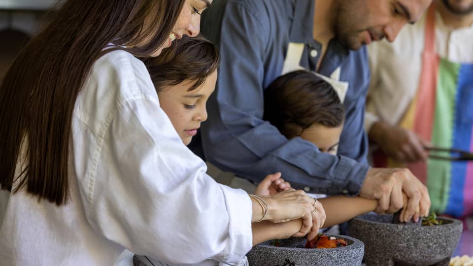 Two adult guests helping two young guests cook.