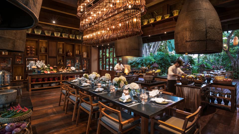 Large dining table under long rectangular crystal chandelier in Rim Tai restaurant, chefs in background