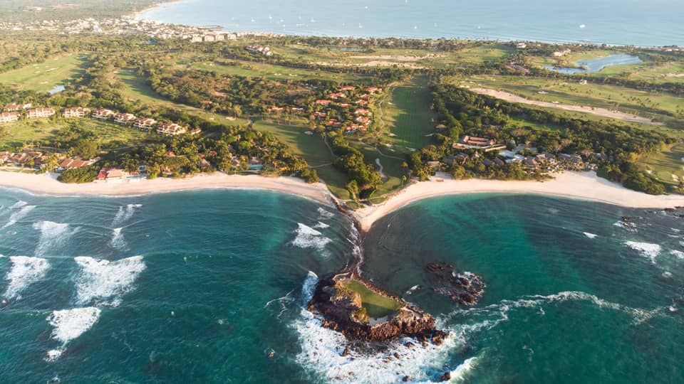 A coastline with deep blue water running up against sand and plants.