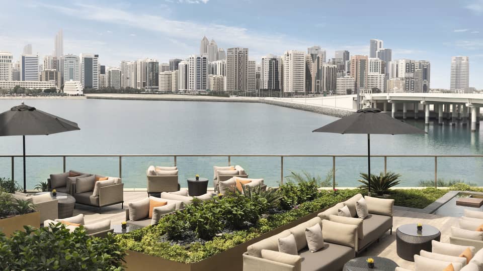 Outdoor sofas, umbrellas and planters on patio overlooking water, city