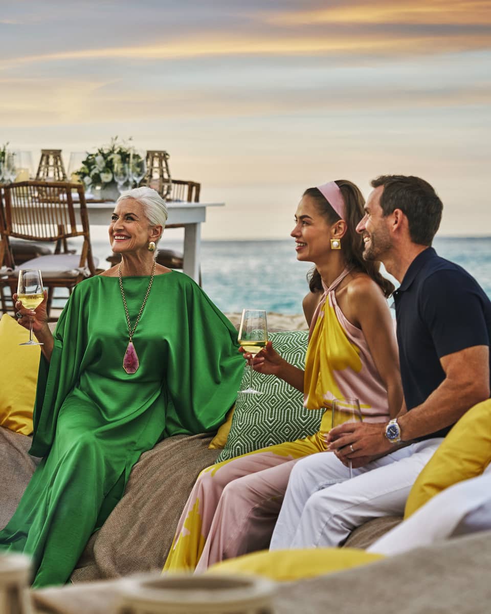 Four guests gathered around a bonfire on the beach and talking to one another.