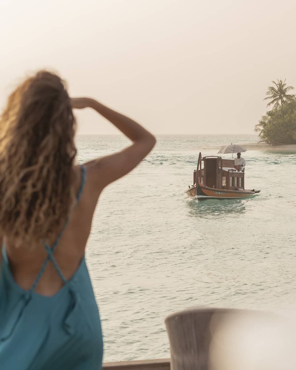Person in blue dress shields eyes as boat travels toward shore