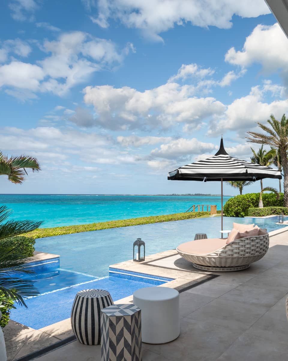 Beachfront villa residence terrace with private infinity pool, sun loungers, and ocean view under a bright blue sky