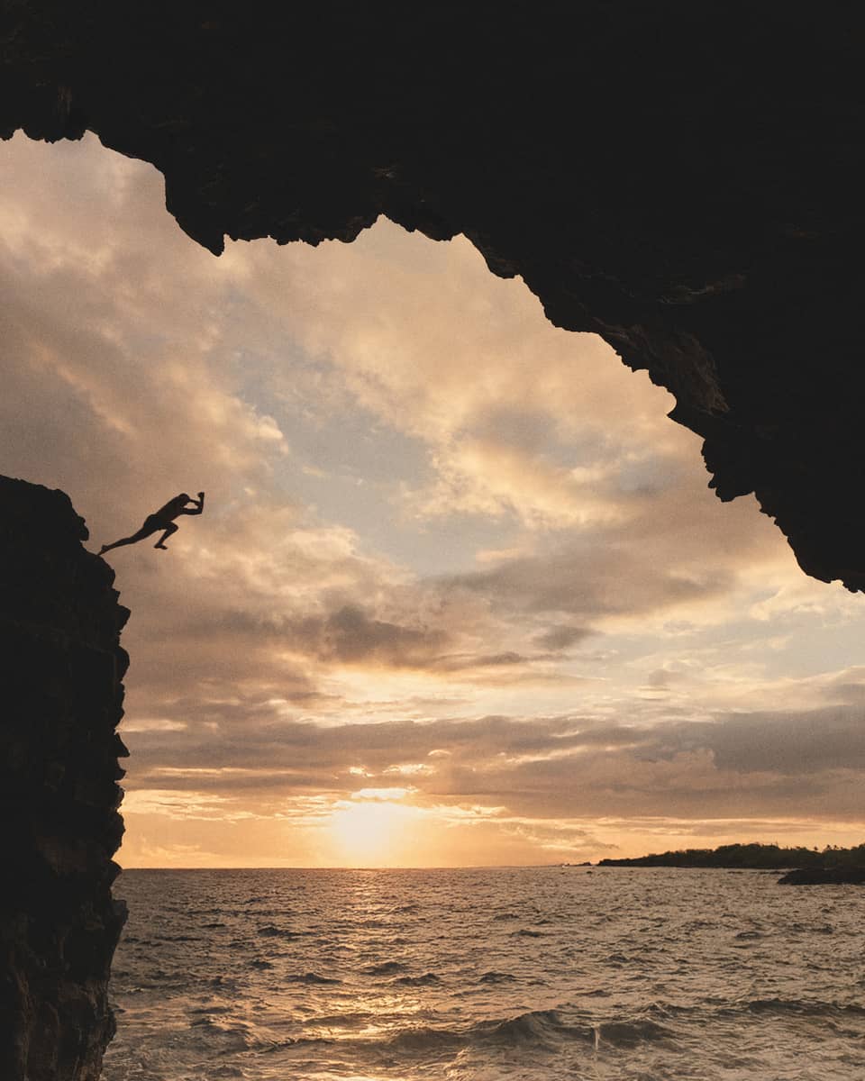 Person jumps off cliff into ocean at sunset in tropical destination