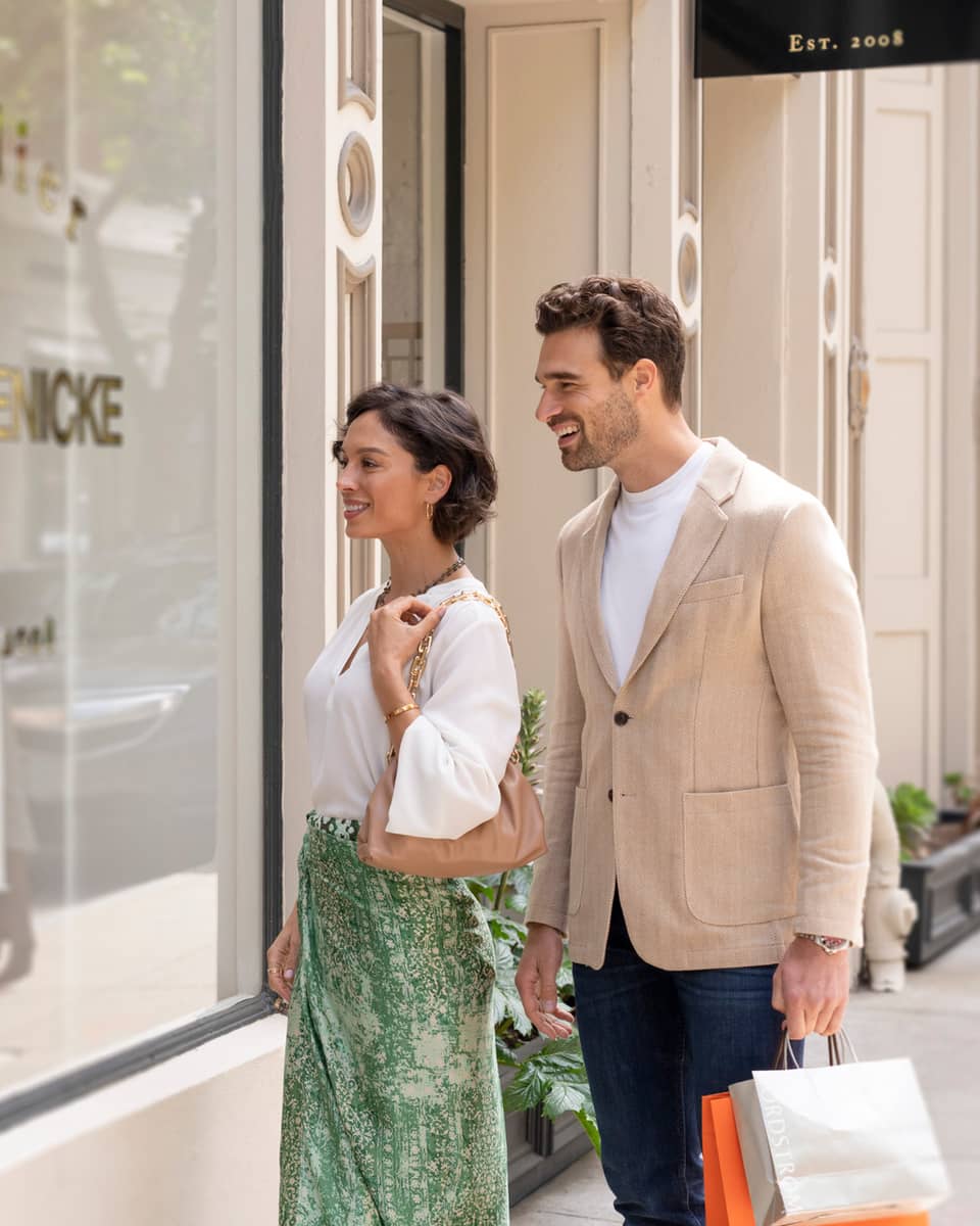 Two people smiling while window shopping in front of a boutique store.