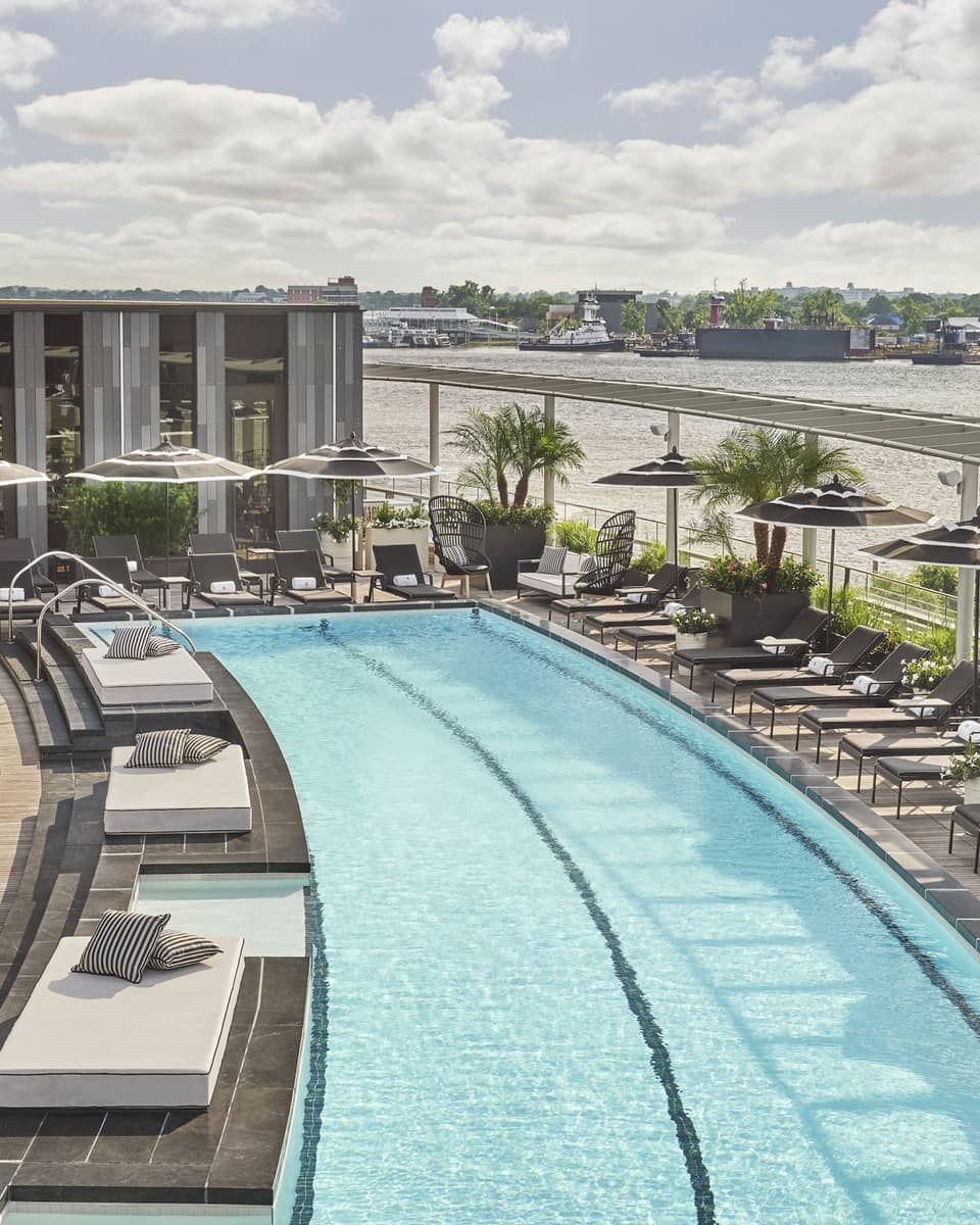 Pool with lounge chairs and umbrellas and a view of the river.