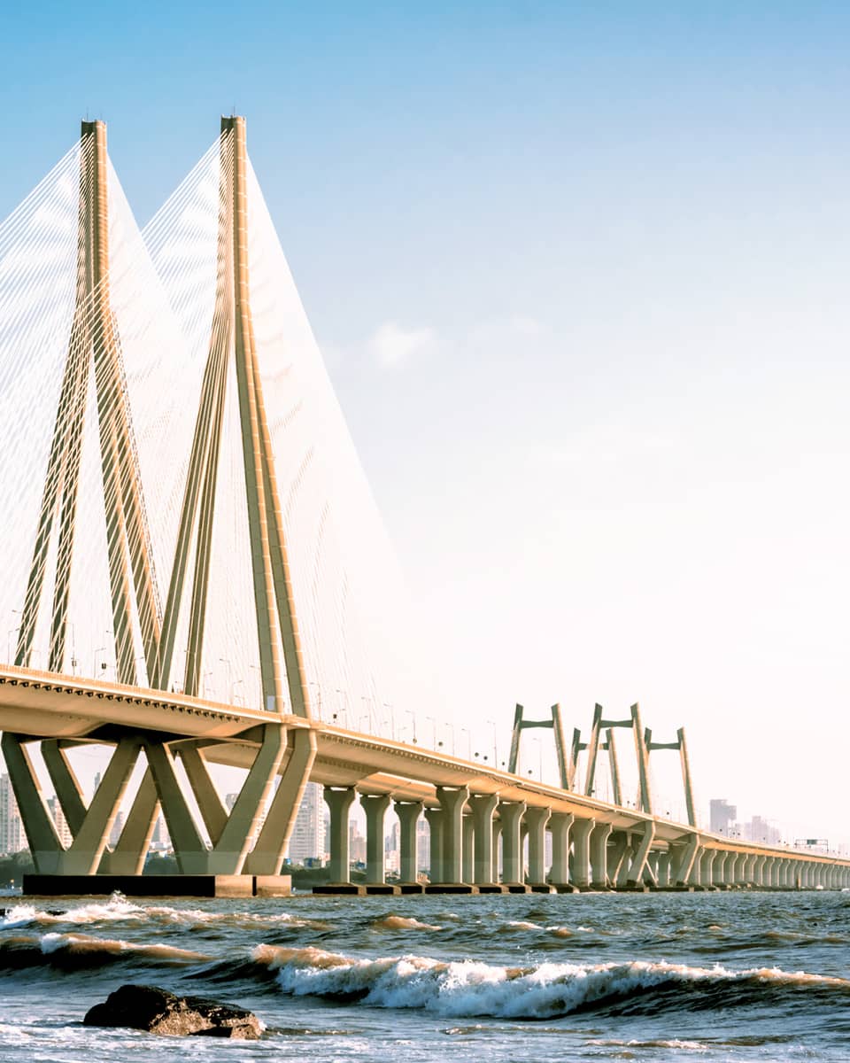View from the water of a kilometres-long bridge featuring a triangular tower connected by scores of luminous steel cables.