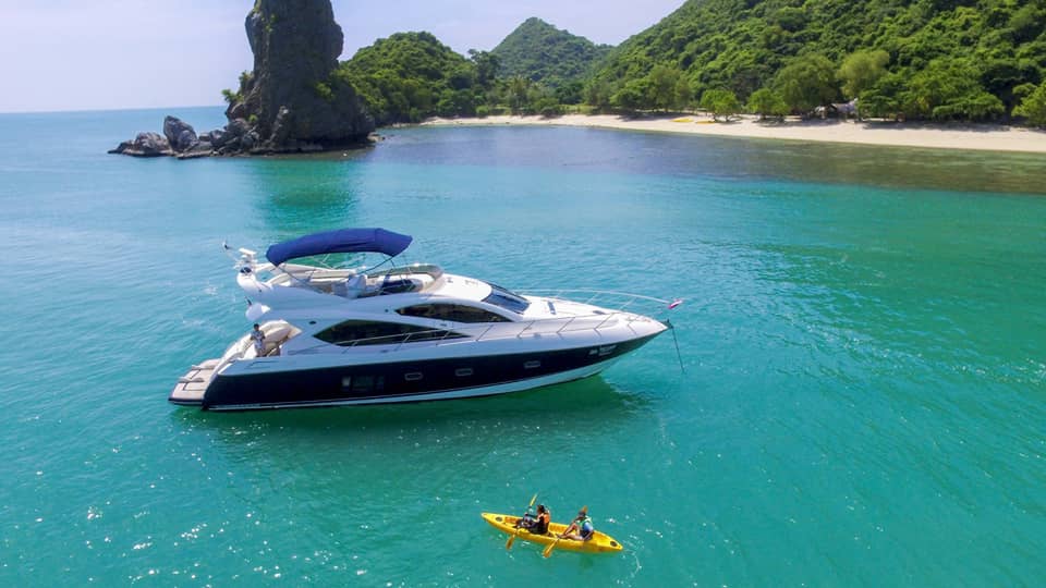 Two people in yellow kayak in front of large white yacht by island in blue ocean
