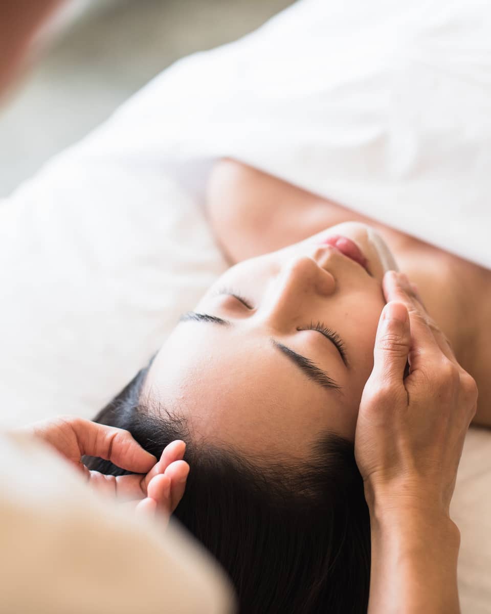 A guest receiving a soothing facial at a spa, lying on a massage table, surrounded by calming décor and soft lighting.