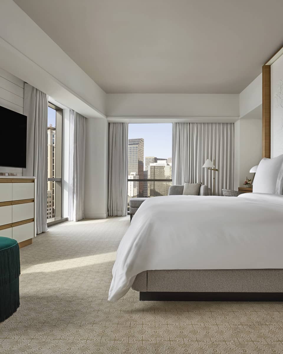 Suite with white king-size bed, flat screen TV, emerald green armchair and floor-to-ceiling windows