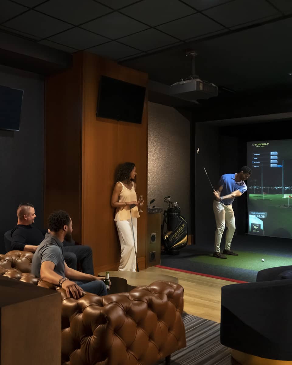 A group of people enjoying an indoor golf simulator experience at the luxury hotel Topgolf Swing Suite, with plush seating and a relaxed atmosphere