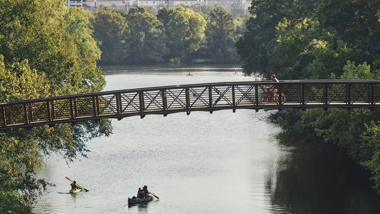 People in kayak, canoe on lake under cyclist on foot bridge