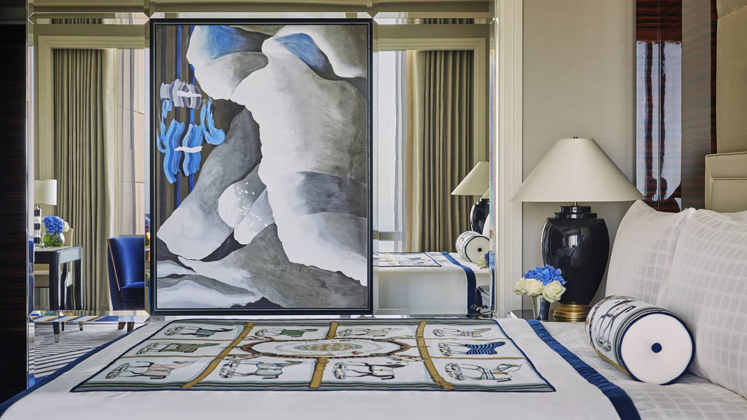 Large modern painting hangs on mirror wall beside bed with decorative blanket