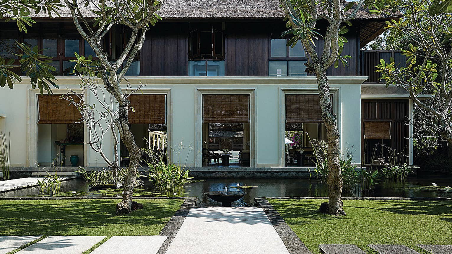 Exterior villa view with pond, small fountain, manicured green lawn, tropical trees