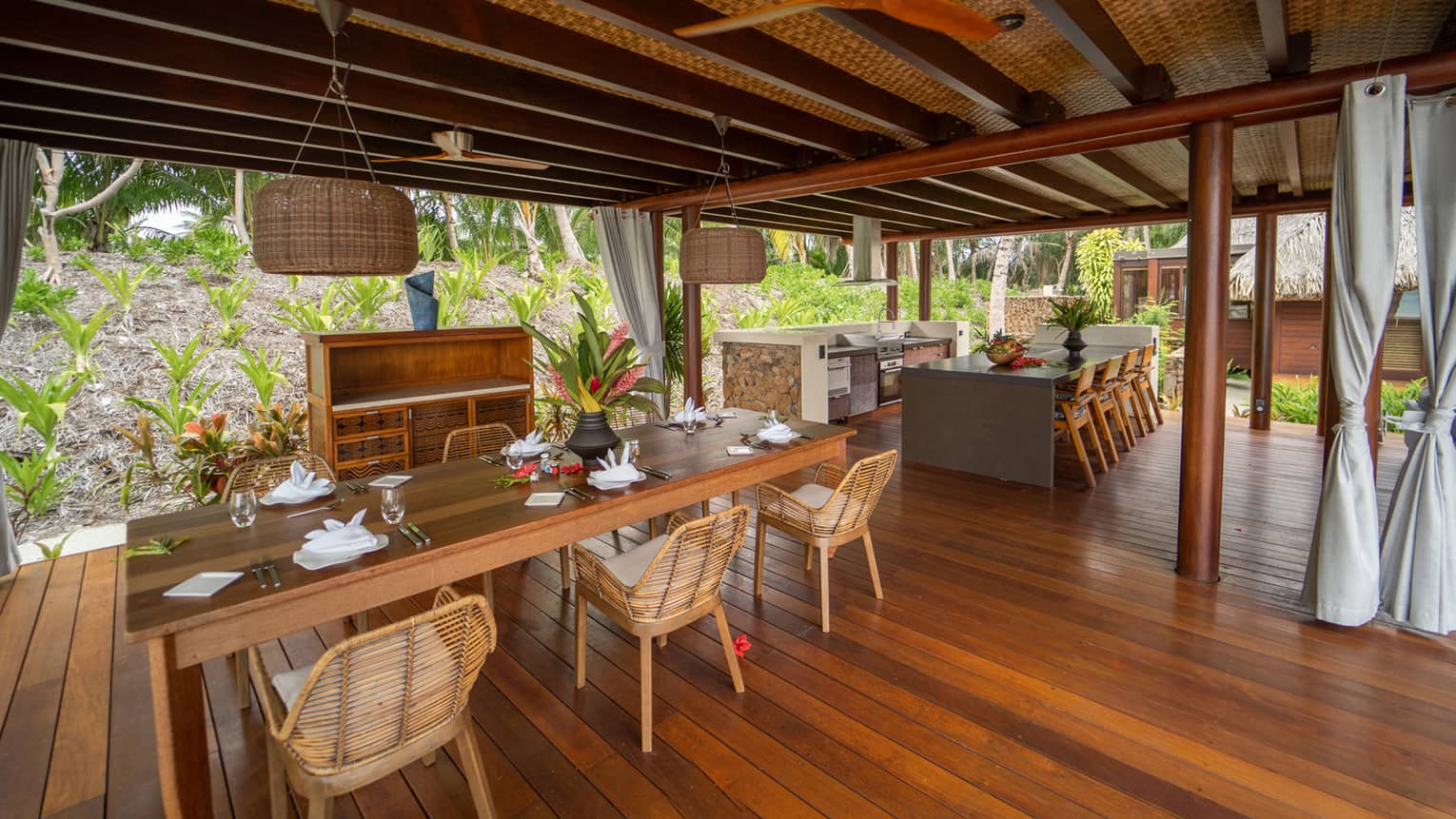 Open-air dining area with wooden floors, bamboo chairs, thatch roof