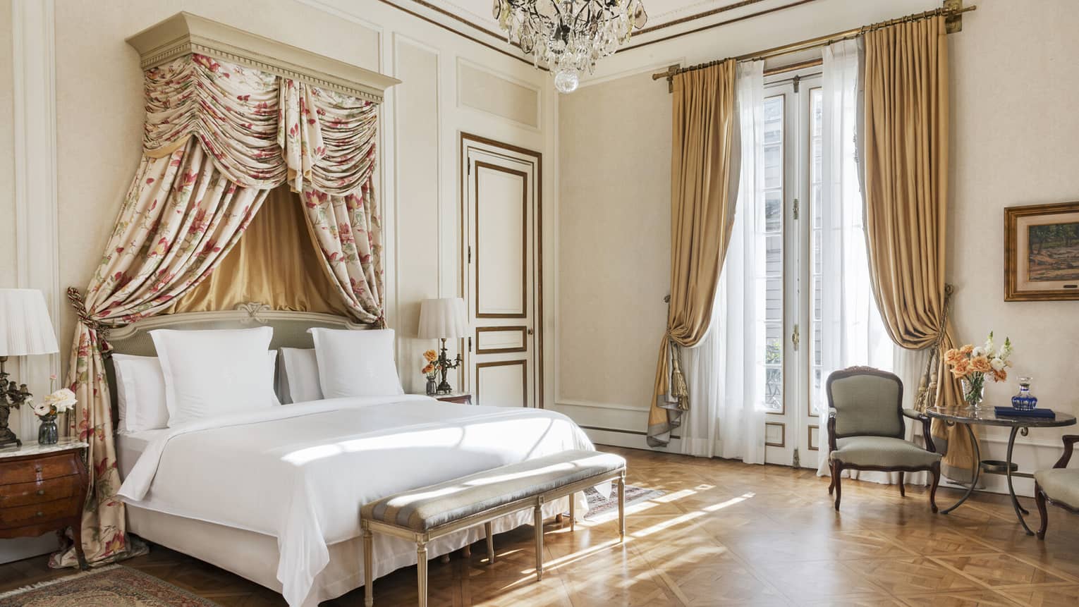 Suite bedroom with parquet floors, tall ceilings and a king-size bed with white linens and a floral canopy headboard