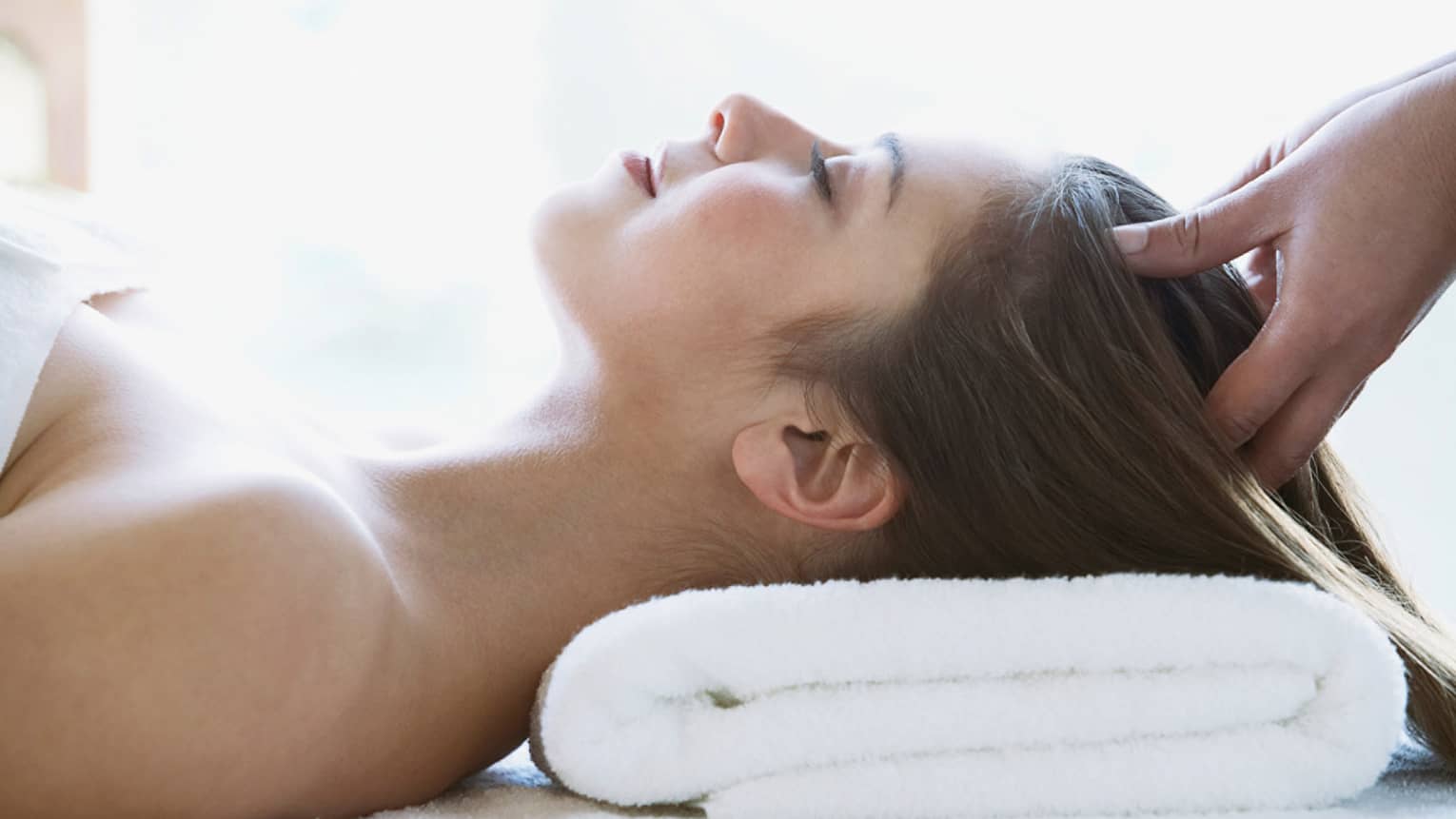Person lying on a spa table receiving a relaxing head massage, with eyes closed and head resting on a white towel.