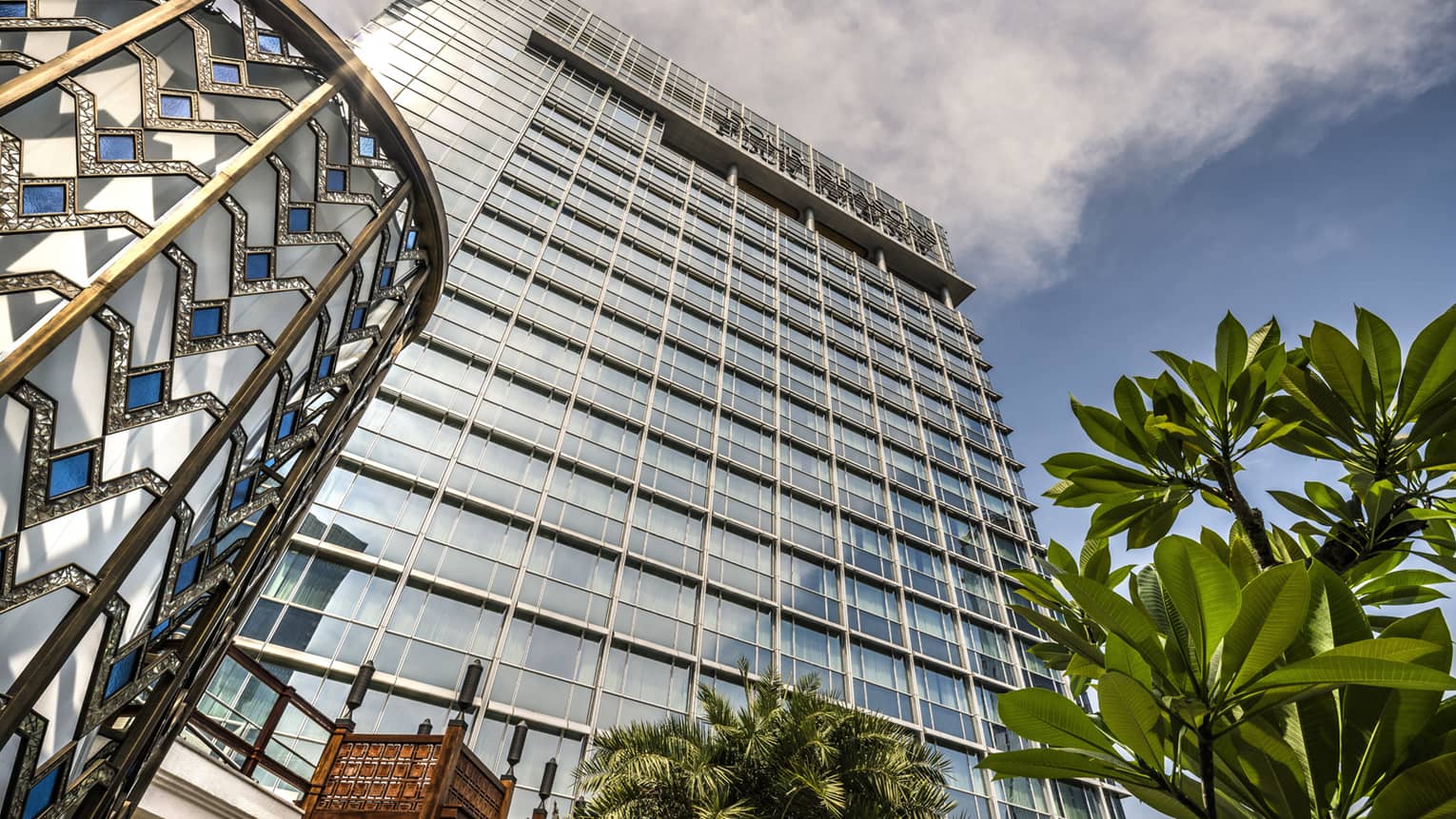 View looking up past tropical plant to glass Four Seasons Hotel Jakarta tower