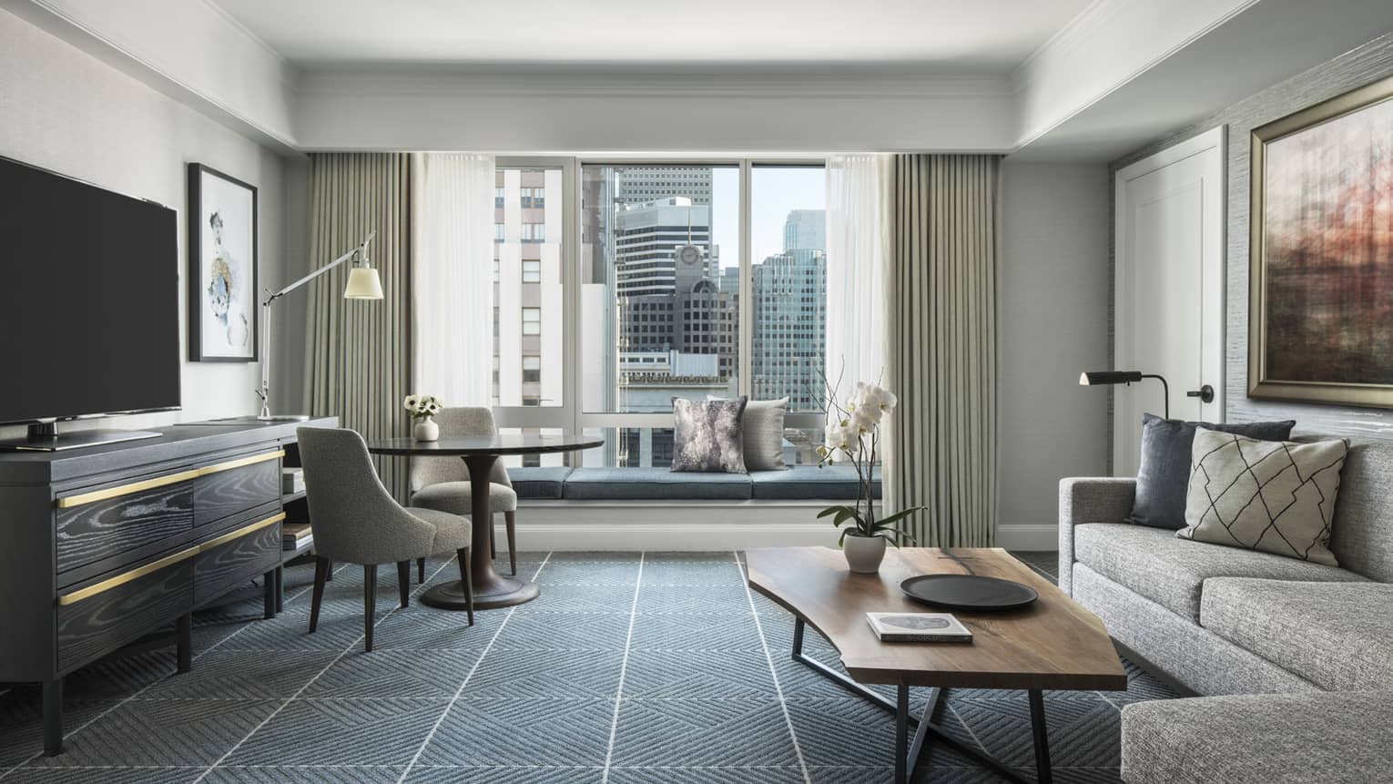 Living room with dark grid-like carpeting, sofa, wooden coffee table, TV, round table and chairs