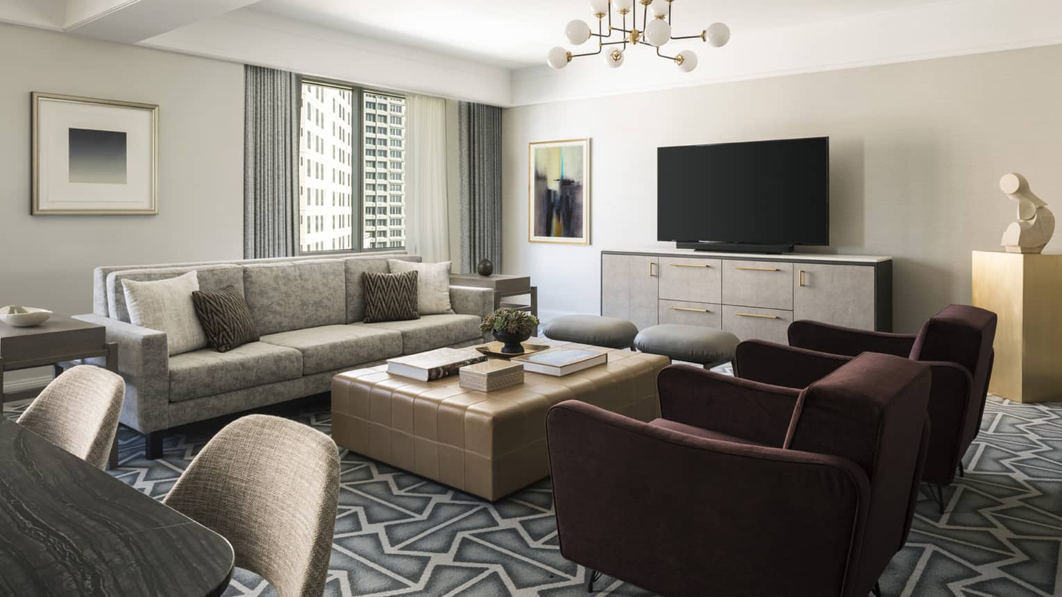 Living room with beige sofa, large square coffee table, two burgundy arm chairs, graphic carpeting