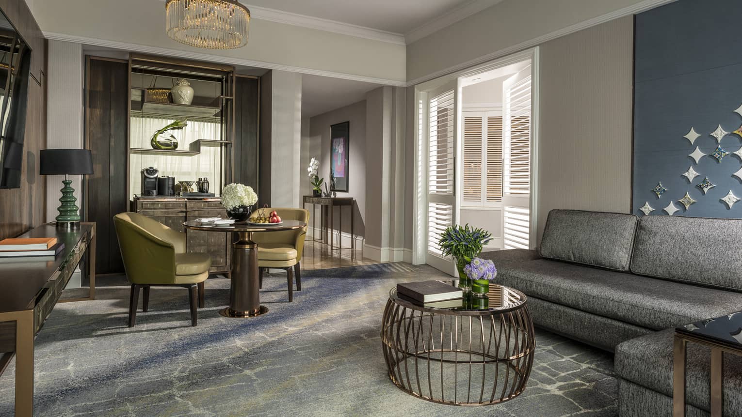 Gold dining chairs around small dining table by brass wire table, L-shaped grey sofa