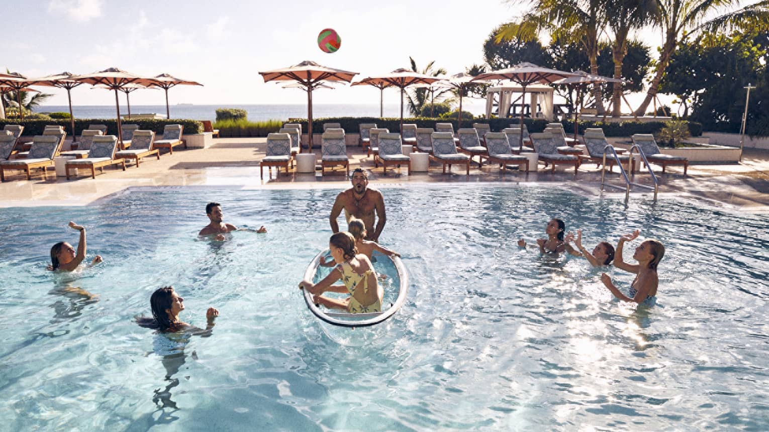 Guests in the pool with palm trees and the ocean in the background.