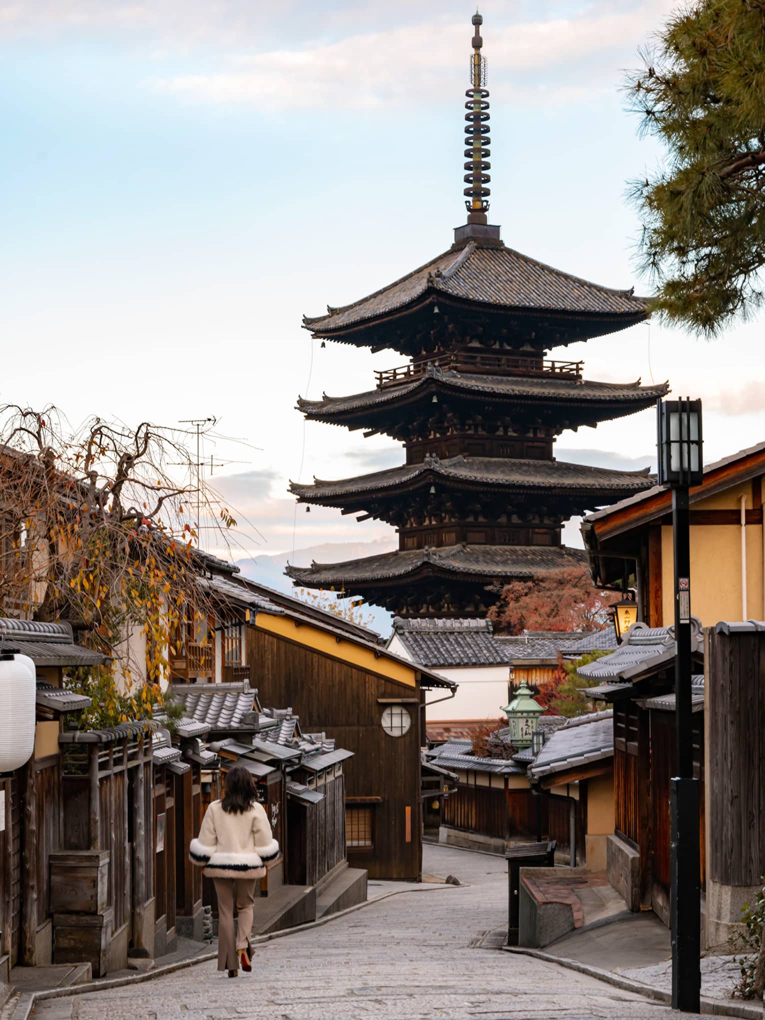 Woman walks down cobblestone street in Kyoto towards Japanese pagoda