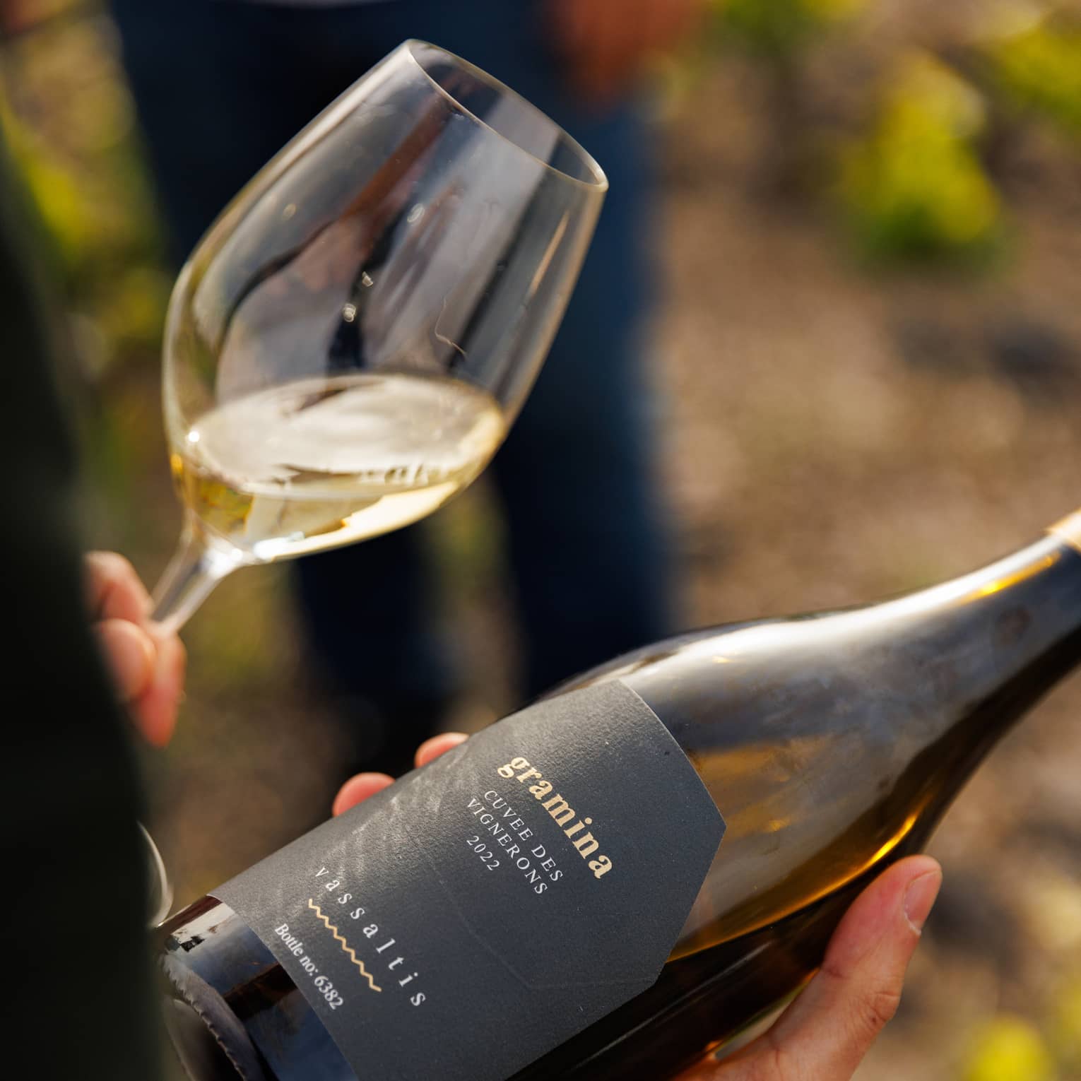 Person holding wine bottle in right hand and glass of white wine in left hand