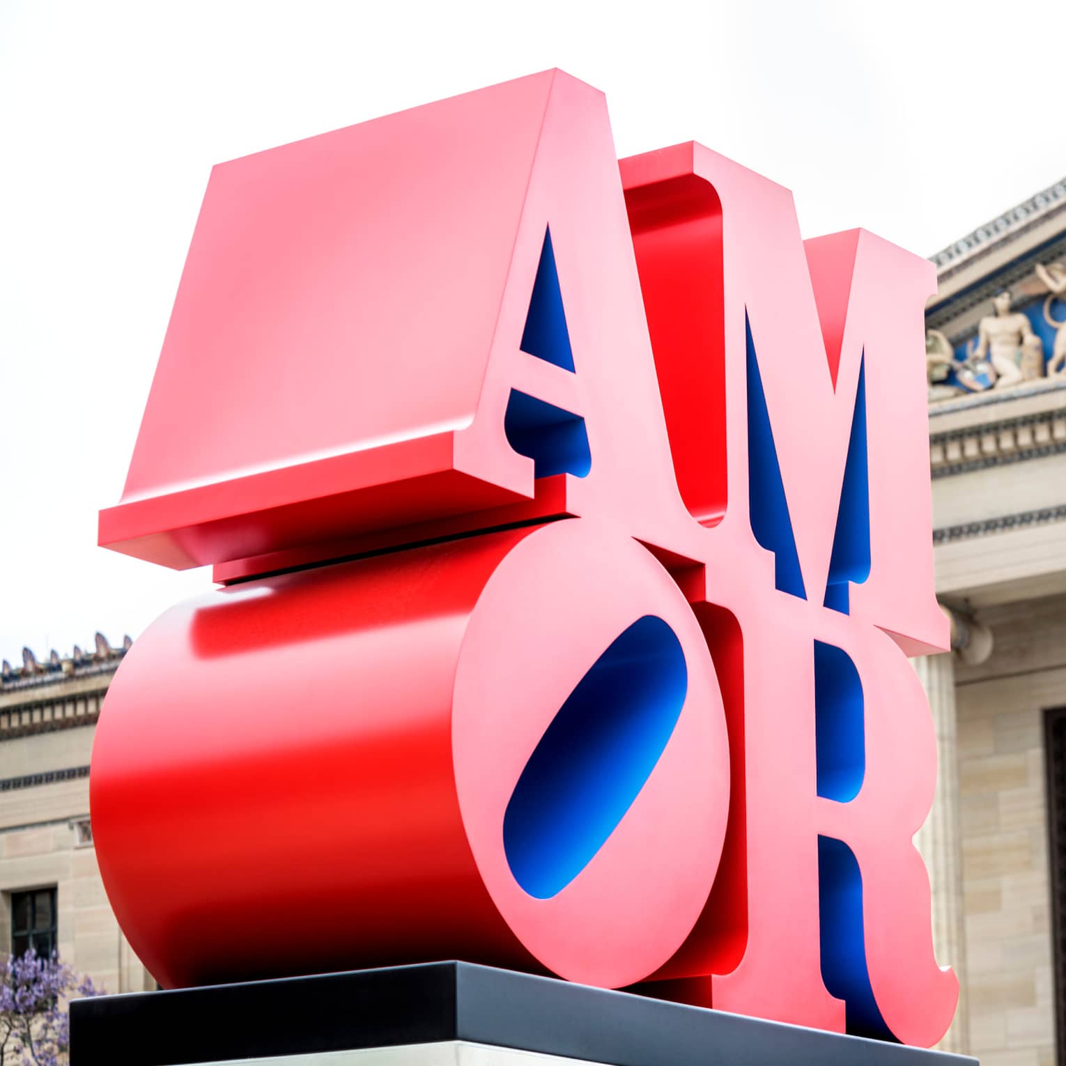Red sculpture spelling AMOR in front of historic building on sunny day