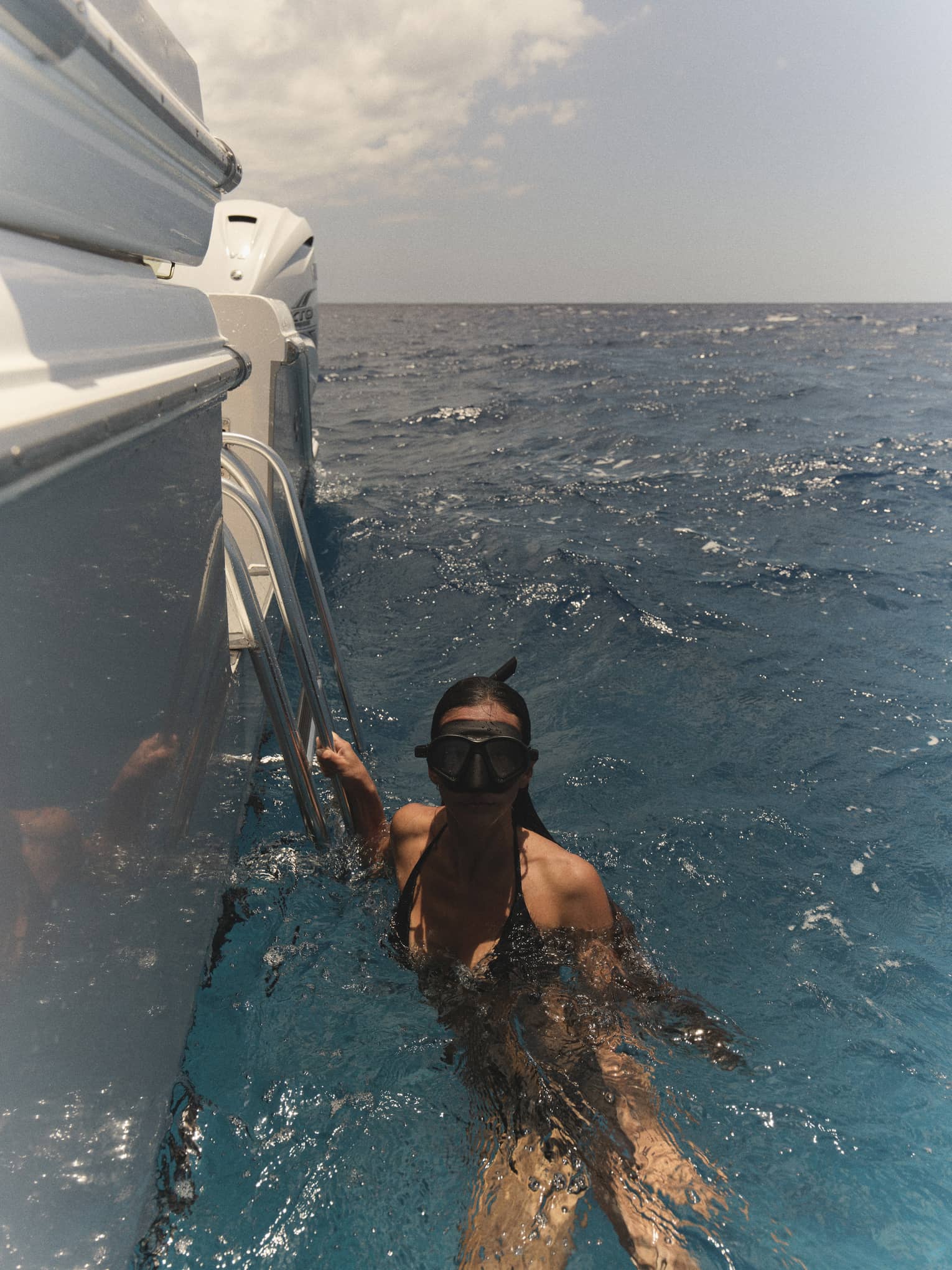 A woman wearing snorkelling goggles holds onto edge of boat in the water
