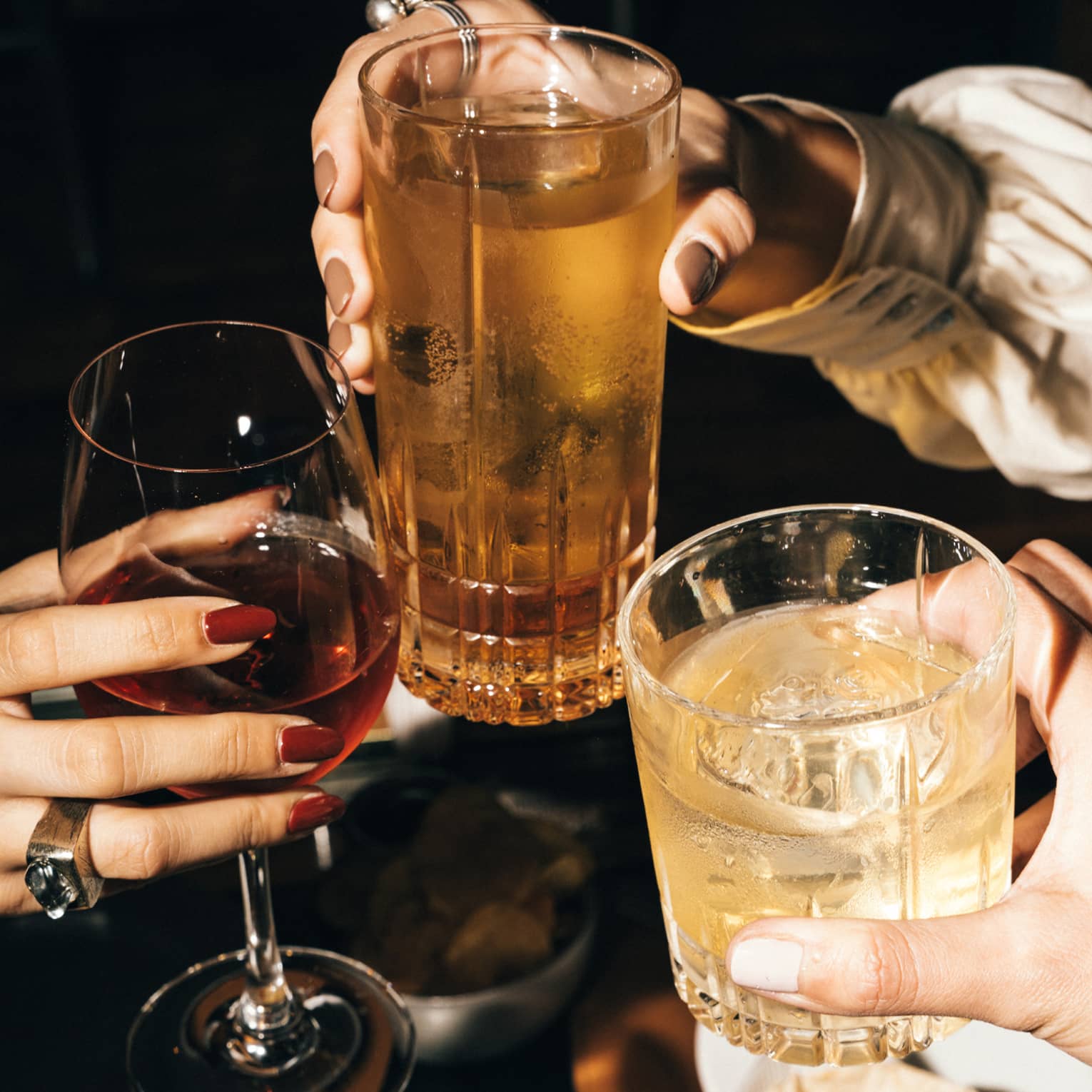 Three hands, each holding a beverage in a glass, bring them together to cheers