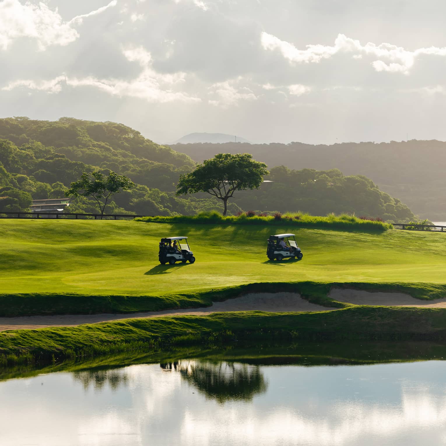 Two golf carts drive along a course next to a water feature