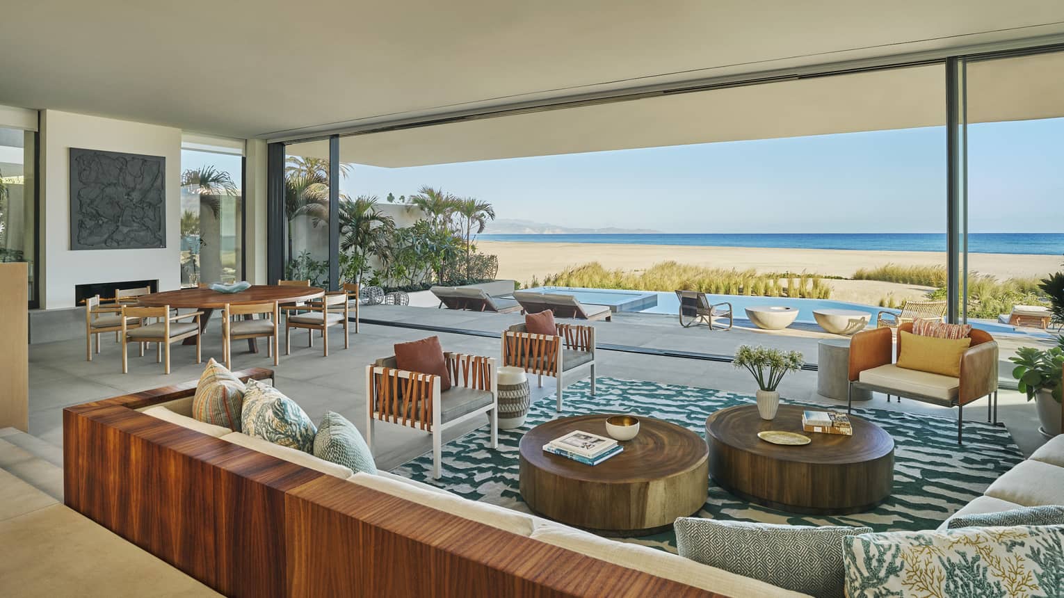 Expansive living and dining room of a private luxury villa with modern Baja design, at Four Seasons Resort and Residences Los Cabos. A huge wall opens to a private pool deck, with sea and beach views.