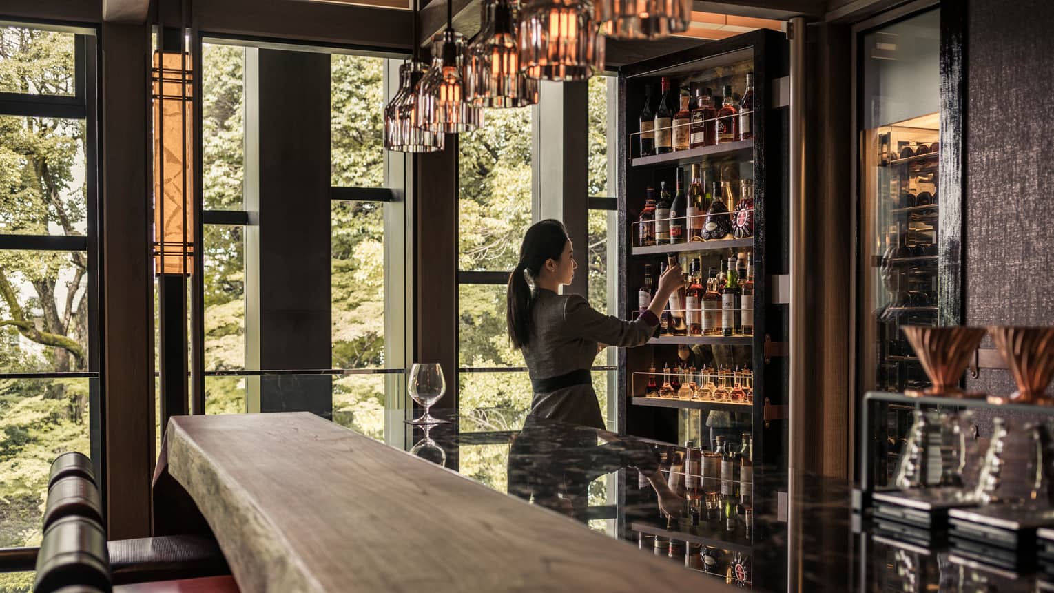 Lounge bartender retrieves bottle on wine from cellar behind long rustic wood bar
