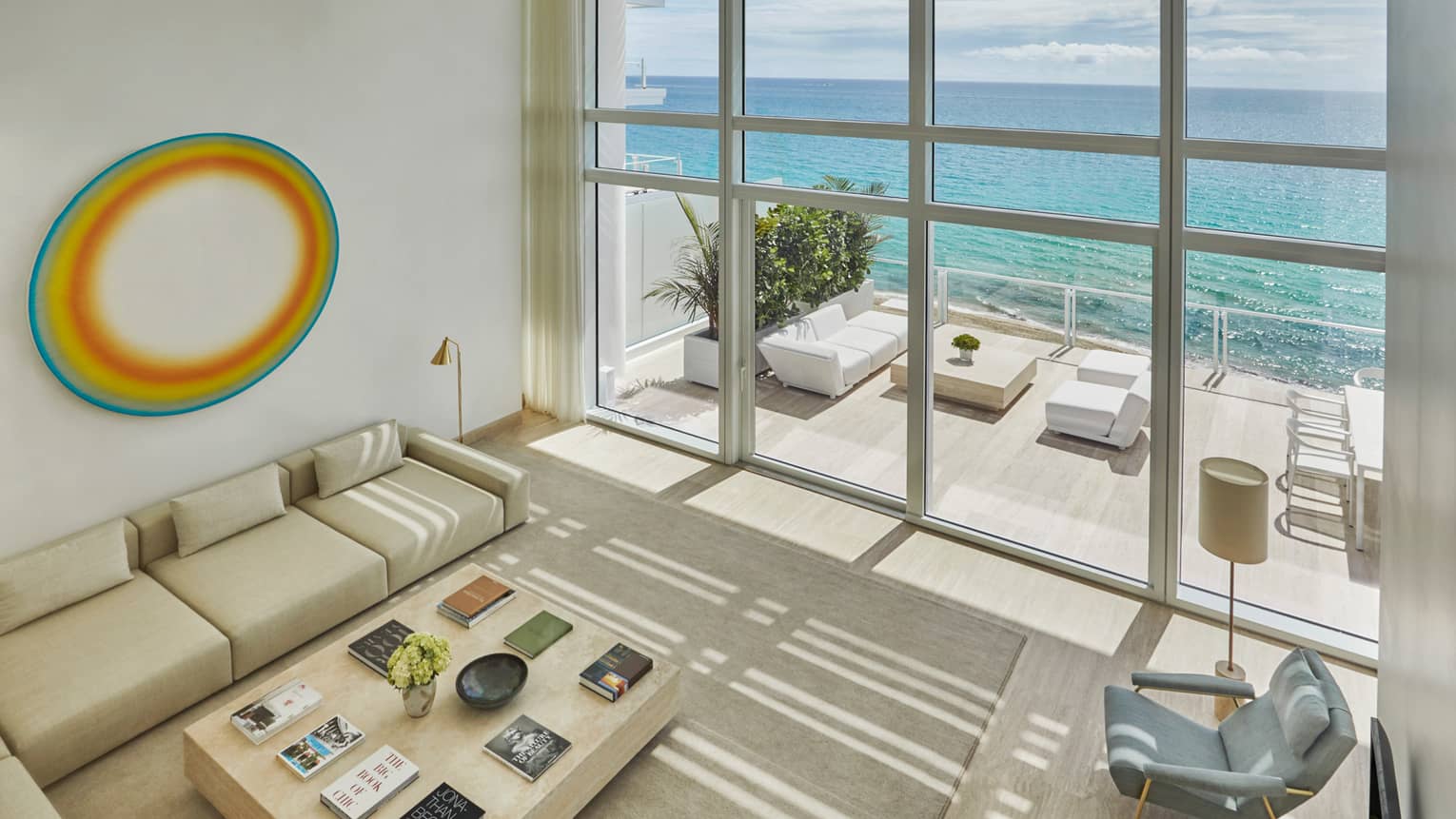 Looking down at bright living room with white L-shaped sofa, armchair, art, glass wall