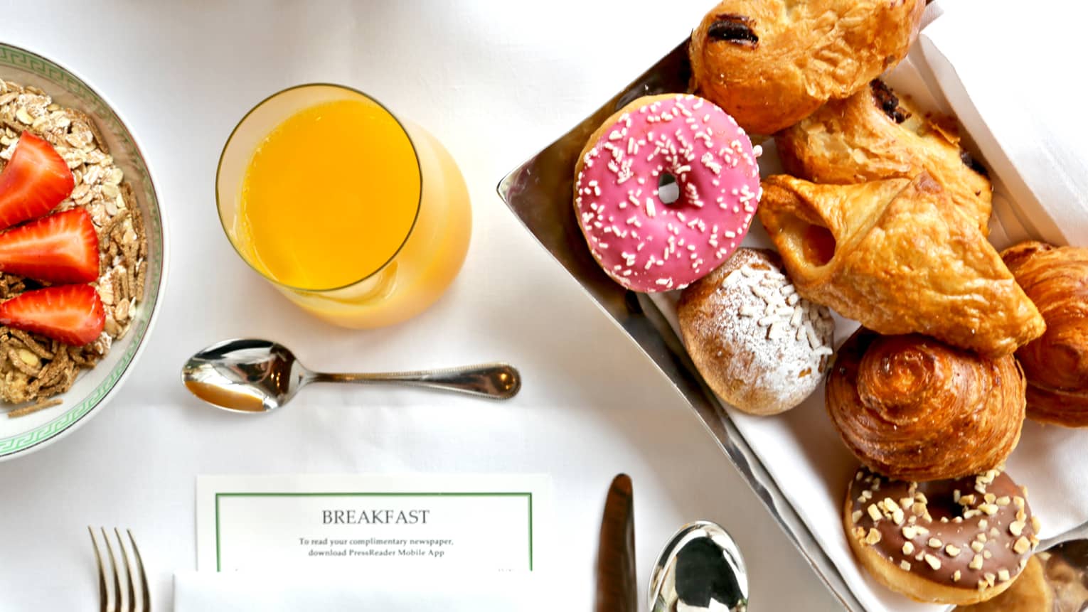 Aerial view of in-room breakfast table with menu, tray with pastries, doughnut with pink icing, orange juice