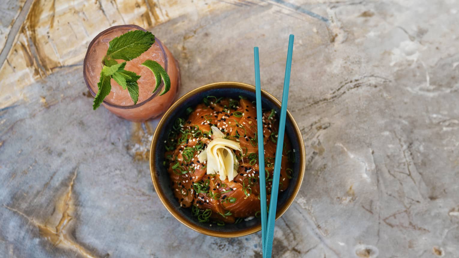 Noodle bowl with blue chopsticks and a pink beverage with lime.