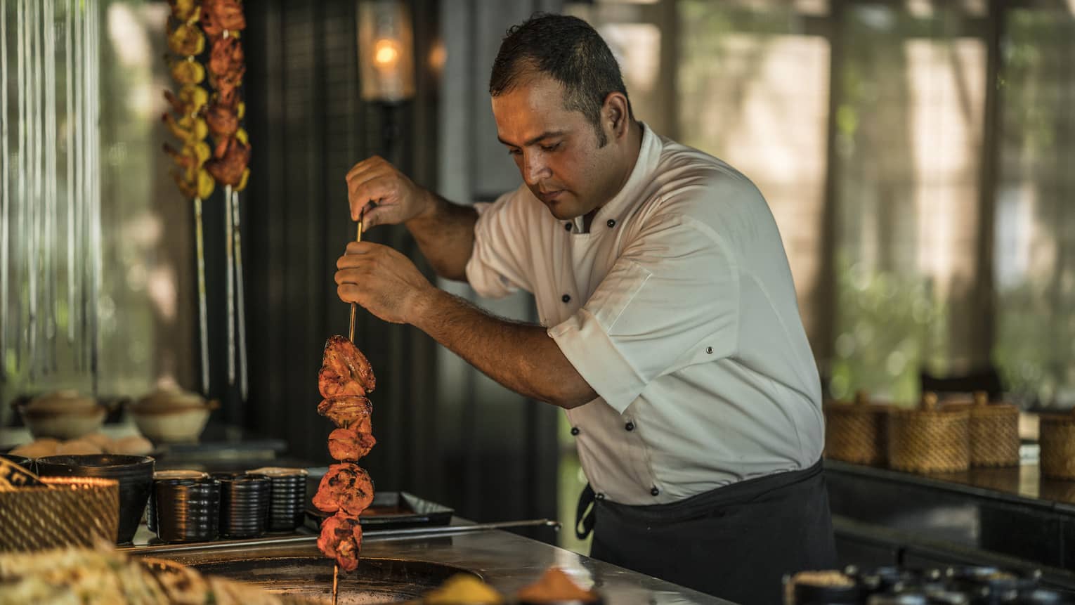 Cafe Nam Hai chef holds skewer with meat over pan