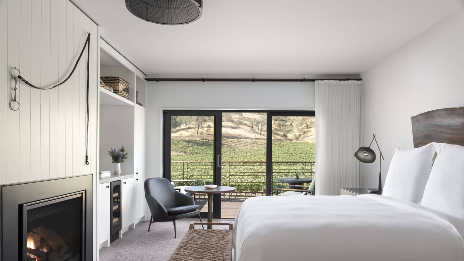 Luxury resort room with a king bed, fireplace, wooden headboard, lounge chair and balcony overlooking vineyard and hillside