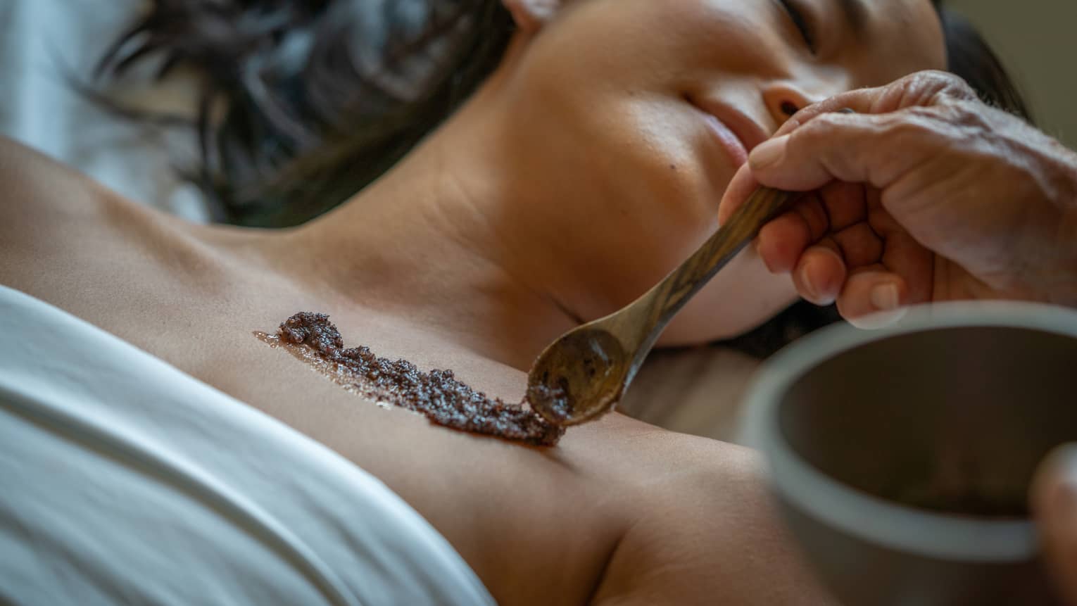 Person laying on a Spa bed while an exfoliating skin scrub is placed on their skin.