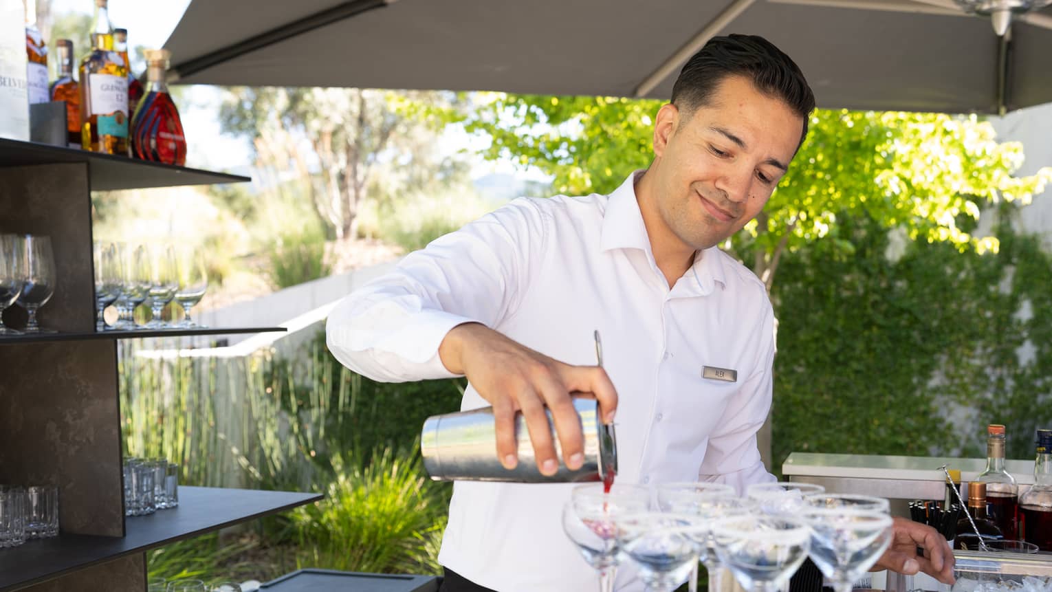 A person wearing a button-down shirt and pouring a drink into glasses