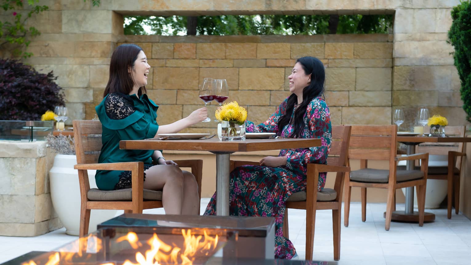 Two guests sitting at an outside dining venue with a fire pit.