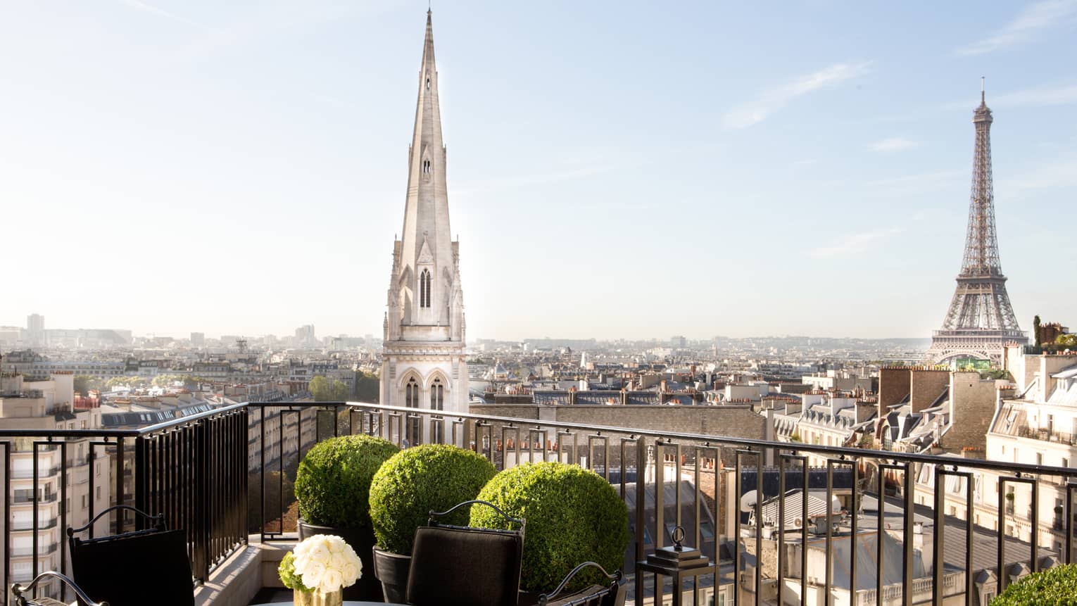 Patio dining table with white roses, potted shrubs iron balcony overlooking Paris rooftops, cathedrals
