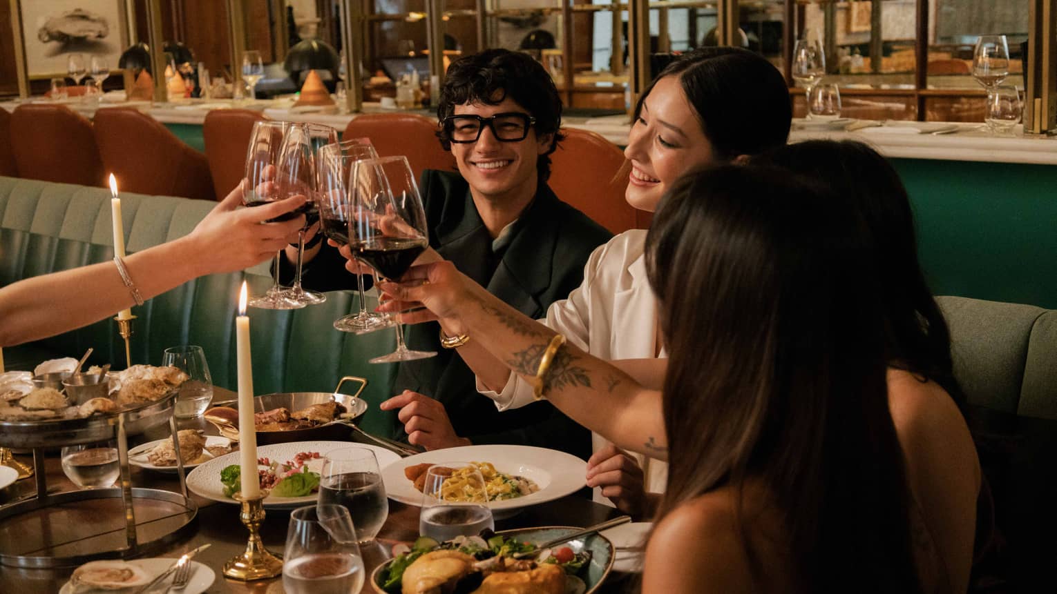 A group clinks glasses of red wine over a dining table filled with various vibrant culinary dishes