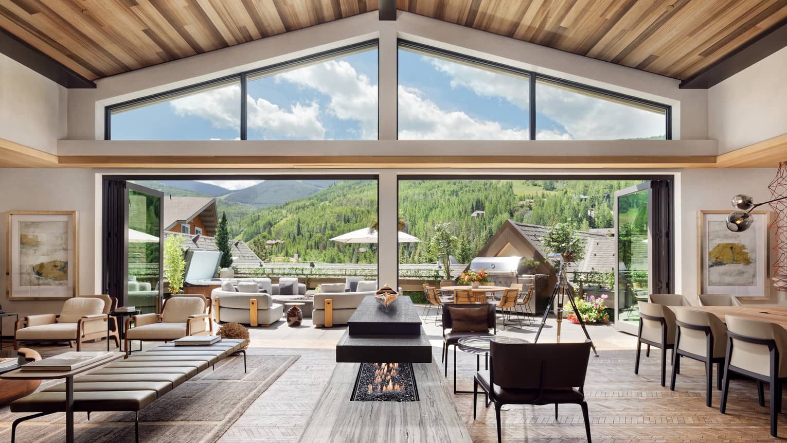 Luxurious mountain villa interior with an open-plan living area, modern fireplace, and expansive glass doors leading to an outdoor terrace with panoramic forest views.