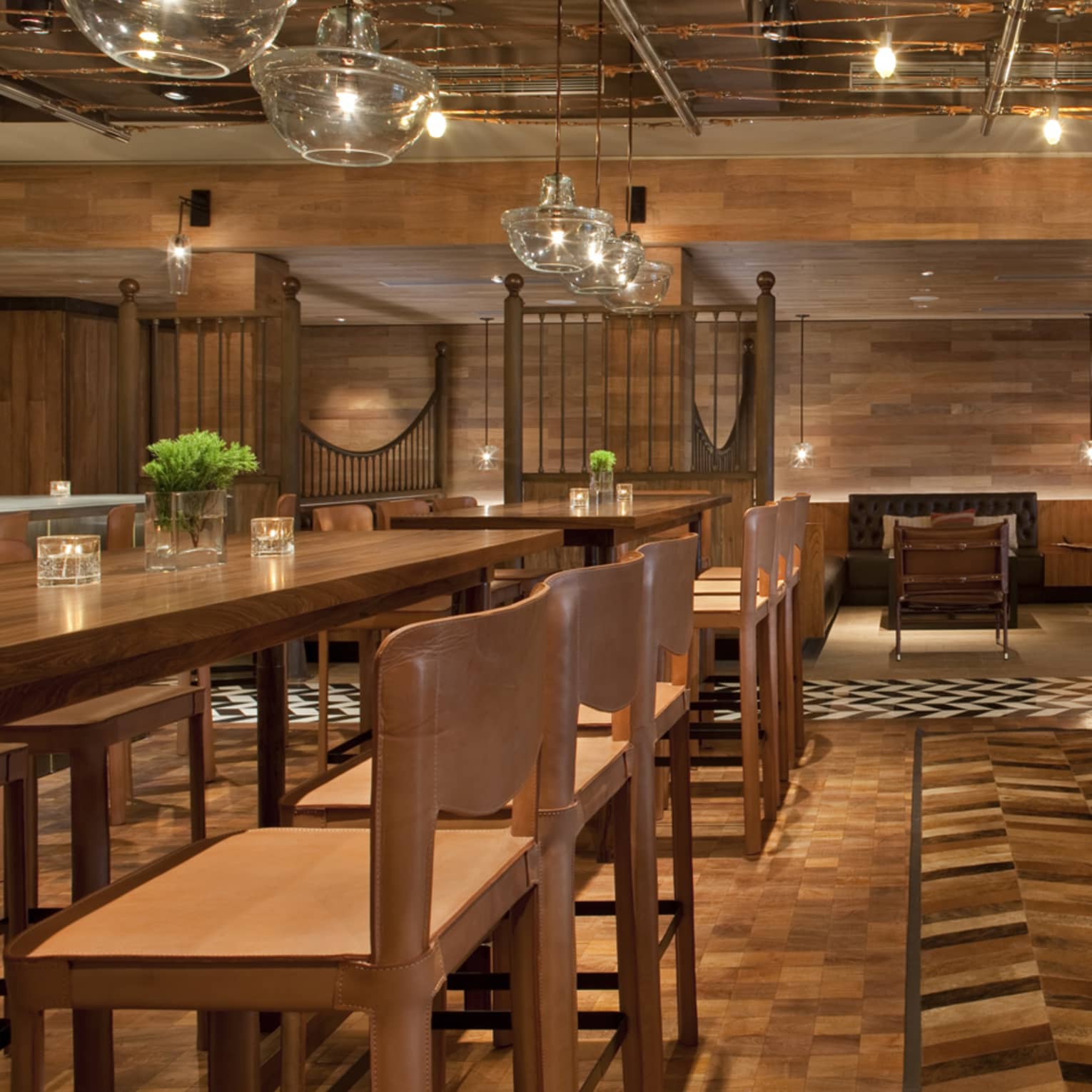 Pony Line lounge with rich brown wood flooring and walls over tables with stools, leather chairs, glass chandeliers